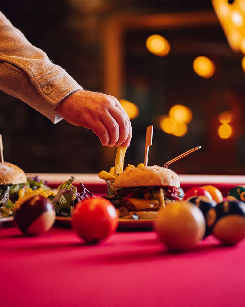 Mini-burgers et frites servis sur le billard, une main pioche une frite
