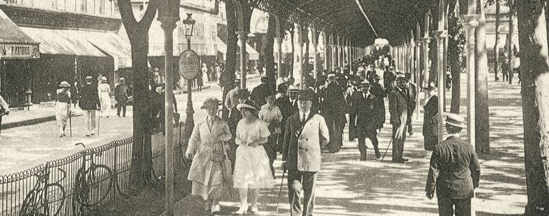Carte postale ancienne : promeneurs sous la galerie couverte du parc des Sources à Vichy