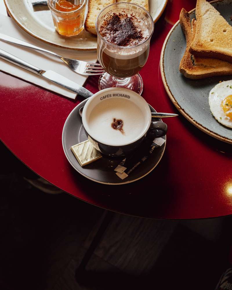 Petit-déjeuner sur une table rouge : café crème, chocolat chaud, tartines grillées et œuf au plat